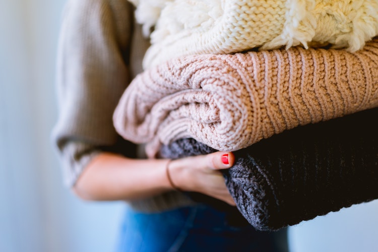 Idei foto de toamnă pentru instagram - o fată cu pulovere pliate în mâini
